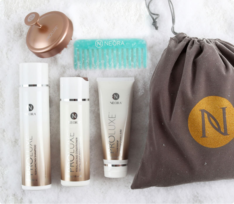 Neora’s hottest holiday must-have, the Get-Gorgeous Holiday Hair Set, which includes ProLuxe™ Rebalancing Shampoo, ProLuxe™ Rebalancing Conditioner, ProLuxe™ Hair Mask, FREE Detangling Comb + FREE Scalp Scrubber and FREE Gift Bag laying on a bed of snow.